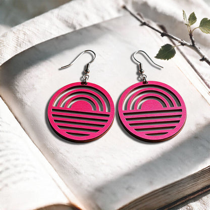 Raspberry Sunrise plywood earrings made in Finland, photographed on a vintage book in natural sunlight