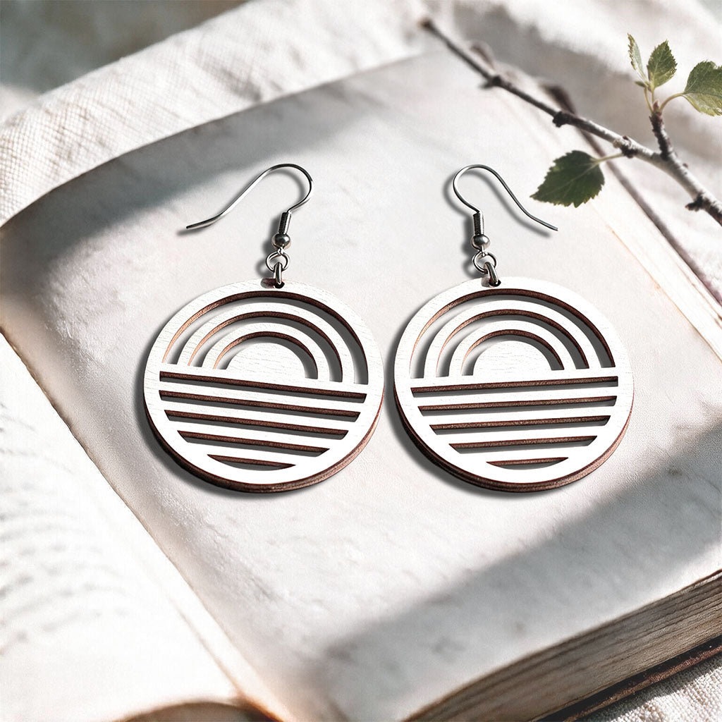 White Sunrise plywood earrings made in Finland, photographed on a vintage book in natural sunlight