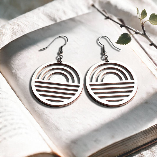 White Sunrise plywood earrings made in Finland, photographed on a vintage book in natural sunlight