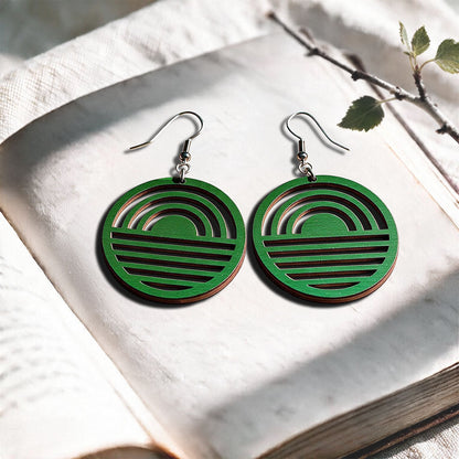 Green Sunrise plywood earrings made in Finland, photographed on a vintage book in natural sunlight