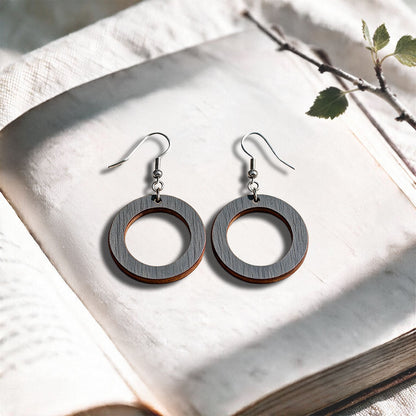 Steel Grey Circle plywood earrings made in Finland, photographed on a vintage book in natural sunlight