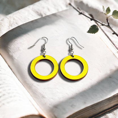 Yellow Circle plywood earrings made in Finland, photographed on a vintage book in natural sunlight