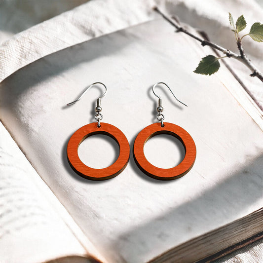 Orange Circle plywood earrings made in Finland, photographed on a vintage book in natural sunlight