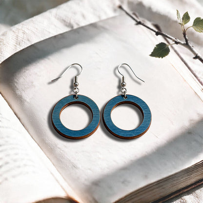 Petrol Blue Circle plywood earrings made in Finland, photographed on a vintage book in natural sunlight
