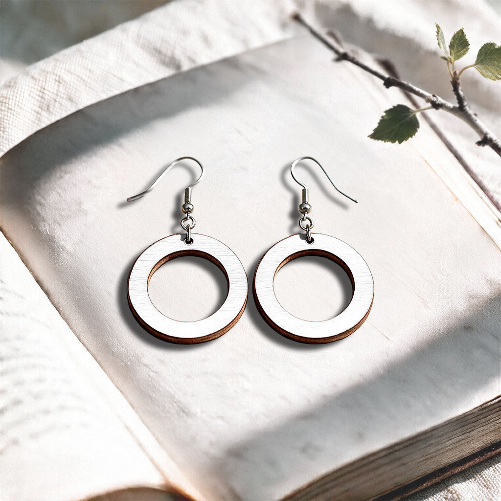 White Circle plywood earrings made in Finland, photographed on a vintage book in natural sunlight