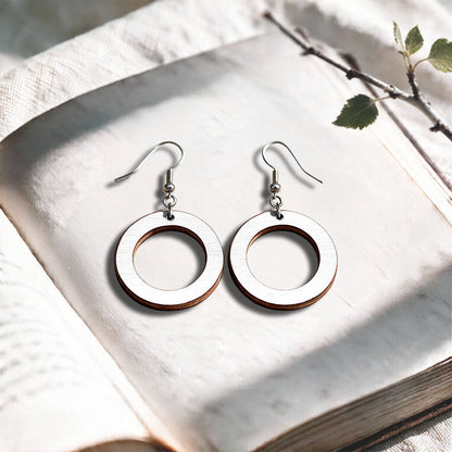 White Circle plywood earrings made in Finland, photographed on a vintage book in natural sunlight