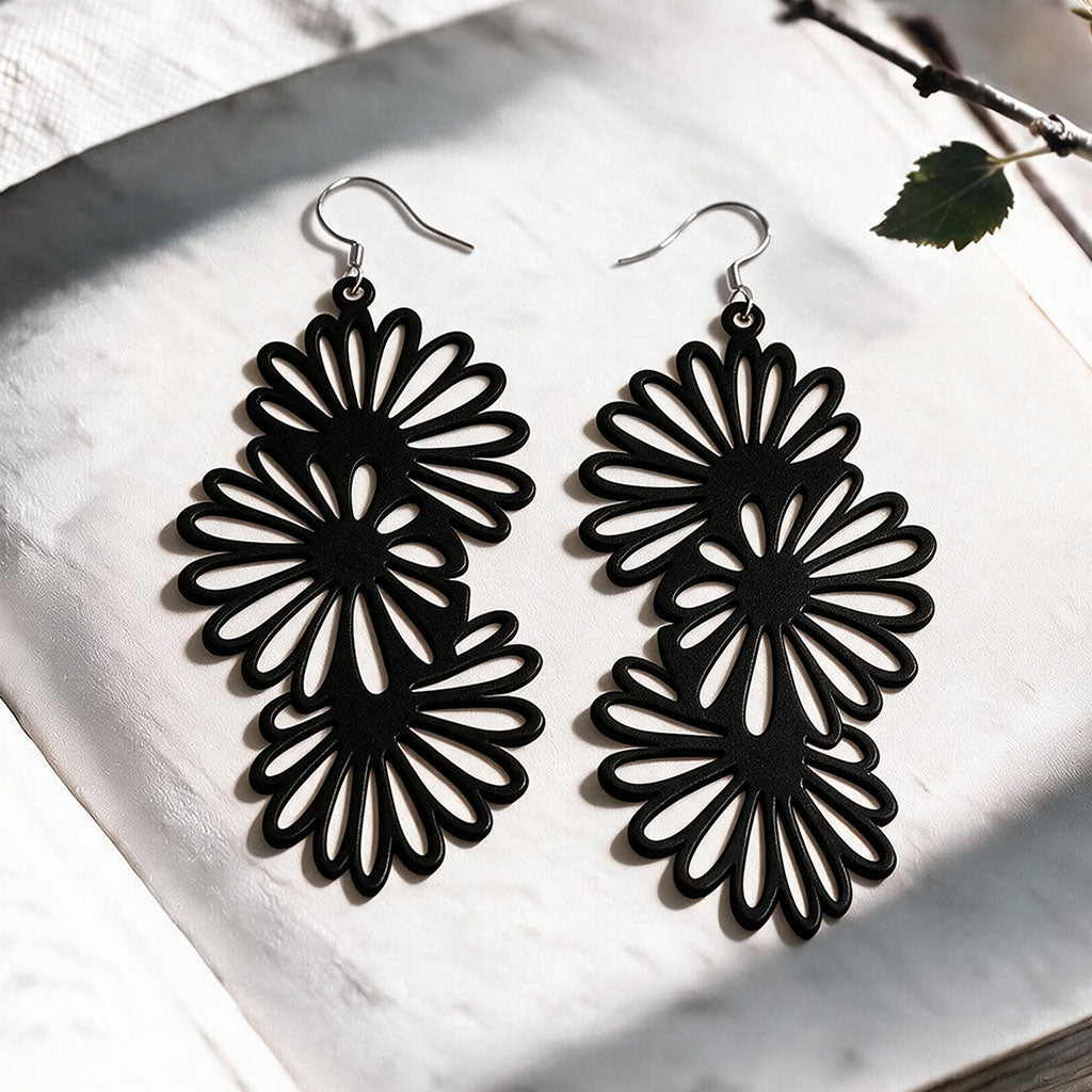 Black Daisy silicone earrings made in Finland, photographed on a vintage book in natural sunlight