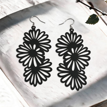 Black Daisy silicone earrings made in Finland, photographed on a vintage book in natural sunlight