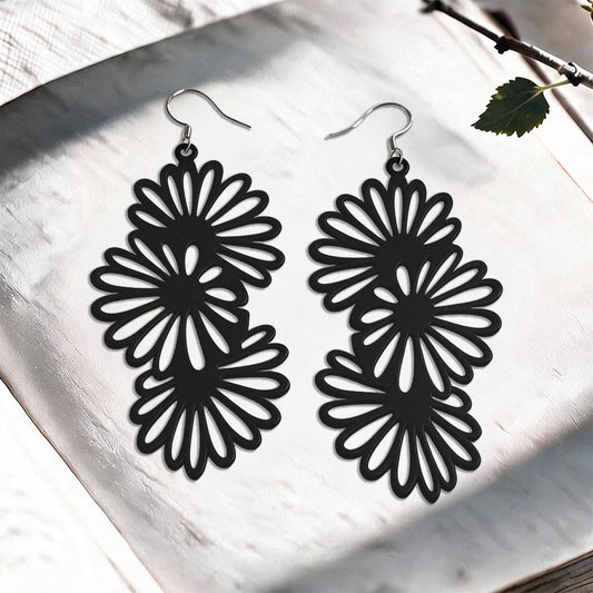 Black Daisy silicone earrings made in Finland, photographed on a vintage book in natural sunlight