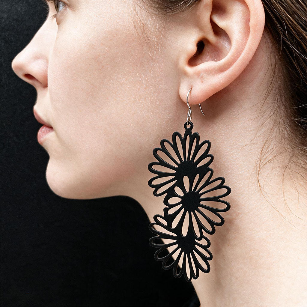 Black Daisy silicone earrings worn on ear, made in Finland