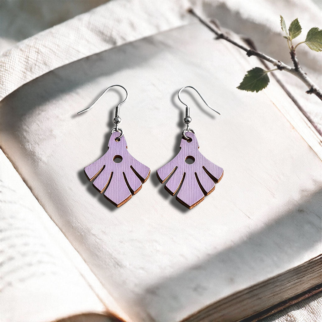 Lavender Phoenix plywood earrings made in Finland, photographed on a vintage book in natural sunlight