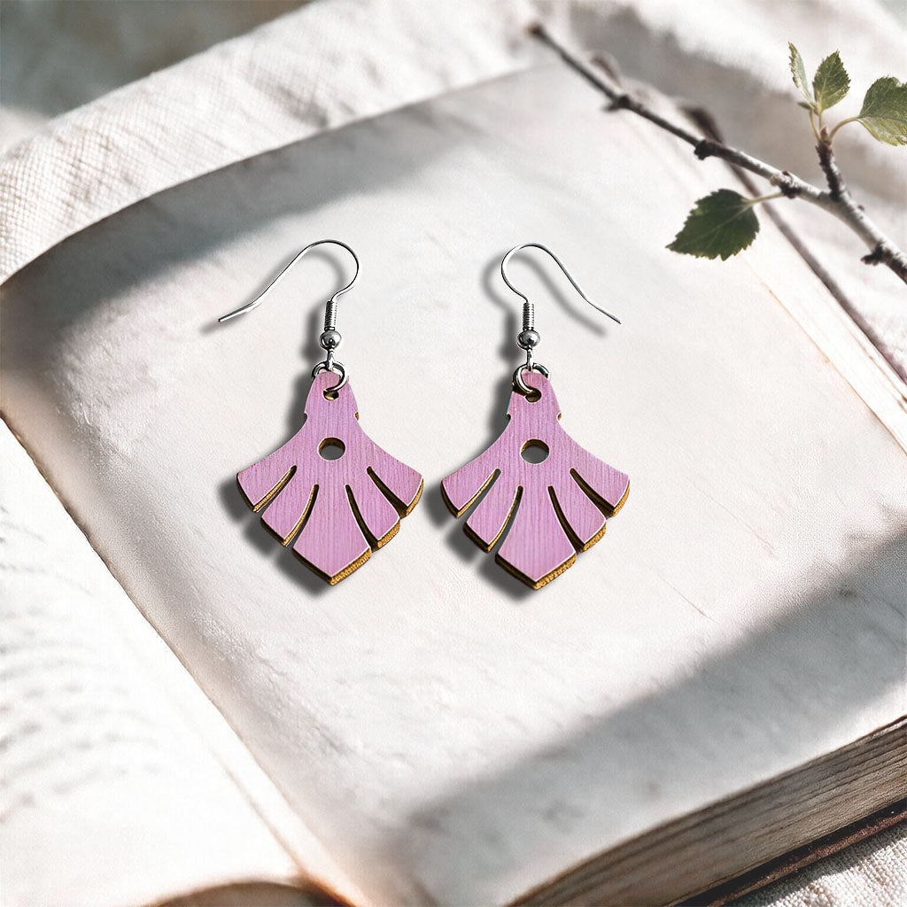 Mauve Phoenix plywood earrings made in Finland, photographed on a vintage book in natural sunlight