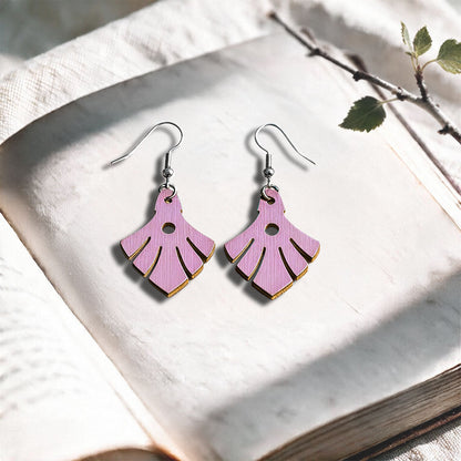Mauve Phoenix plywood earrings made in Finland, photographed on a vintage book in natural sunlight