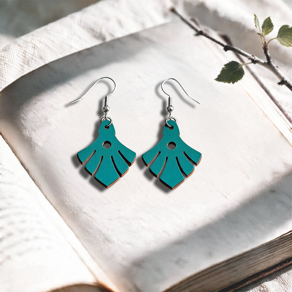 Petrol Phoenix plywood earrings made in Finland, photographed on a vintage book in natural sunlight