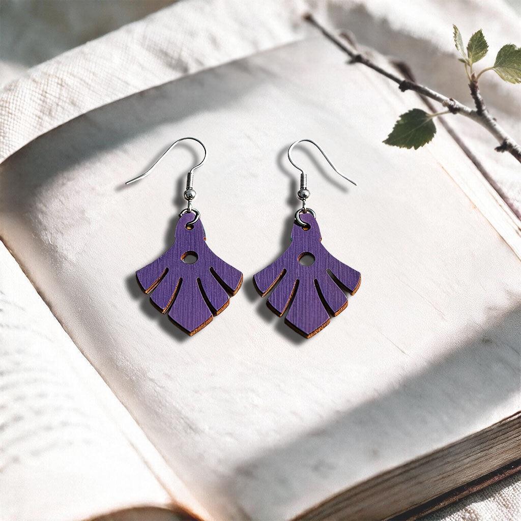 Plum Phoenix plywood earrings made in Finland, photographed on a vintage book in natural sunlight