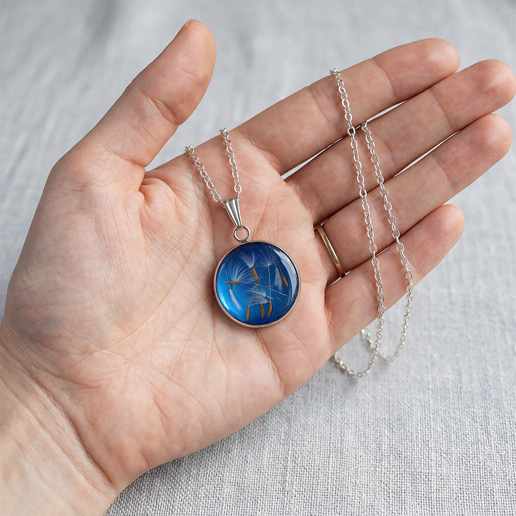 Hand holding handmade dandelion seed necklace with real dandelion seeds preserved in resin