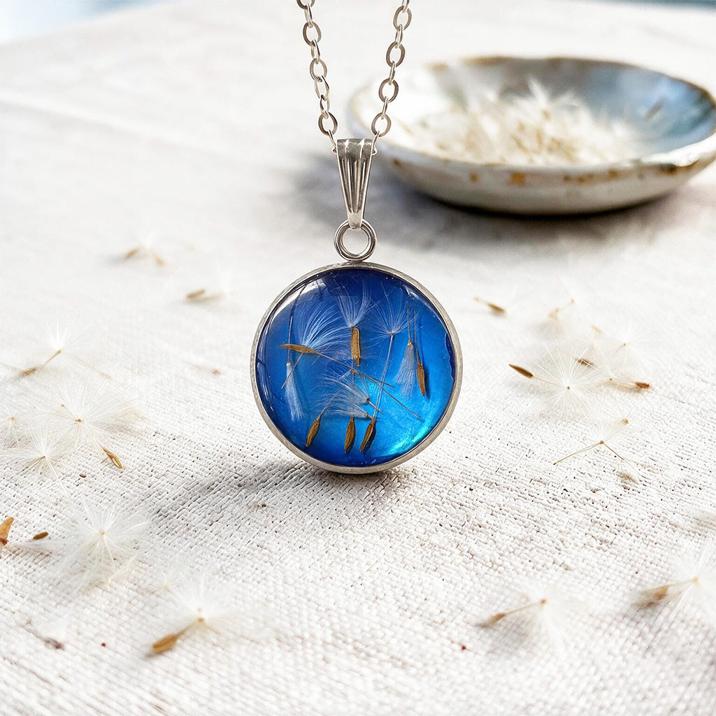 Dandelion seed necklace with real dandelion seeds preserved in resin, photographed on a linen background with natural botanical details.