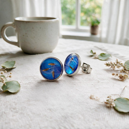 Dandelion seed stud earrings with real dandelion seeds preserved in resin, photographed on a linen background with natural botanical details.