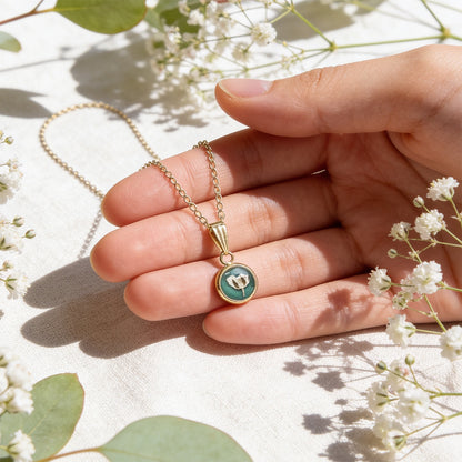 Hand holding a handmade botanical necklace for size reference, surrounded by delicate baby's breath flowers and soft green eucalyptus leaves in bright natural daylight. Elegant product photography with a light linen background.