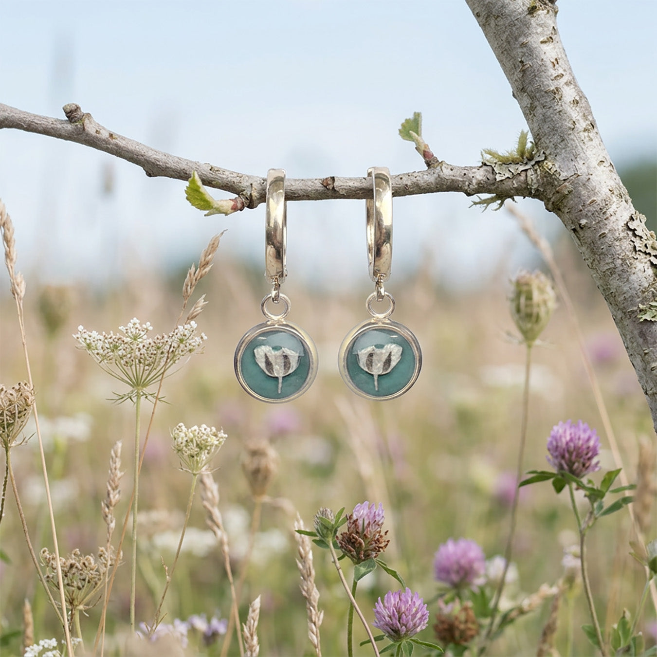 Sage green botanical huggie earrings hanging from tree branch in wildflower meadow