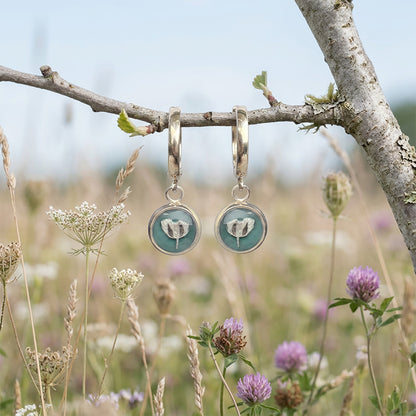 Sage green botanical huggie earrings hanging from tree branch in wildflower meadow