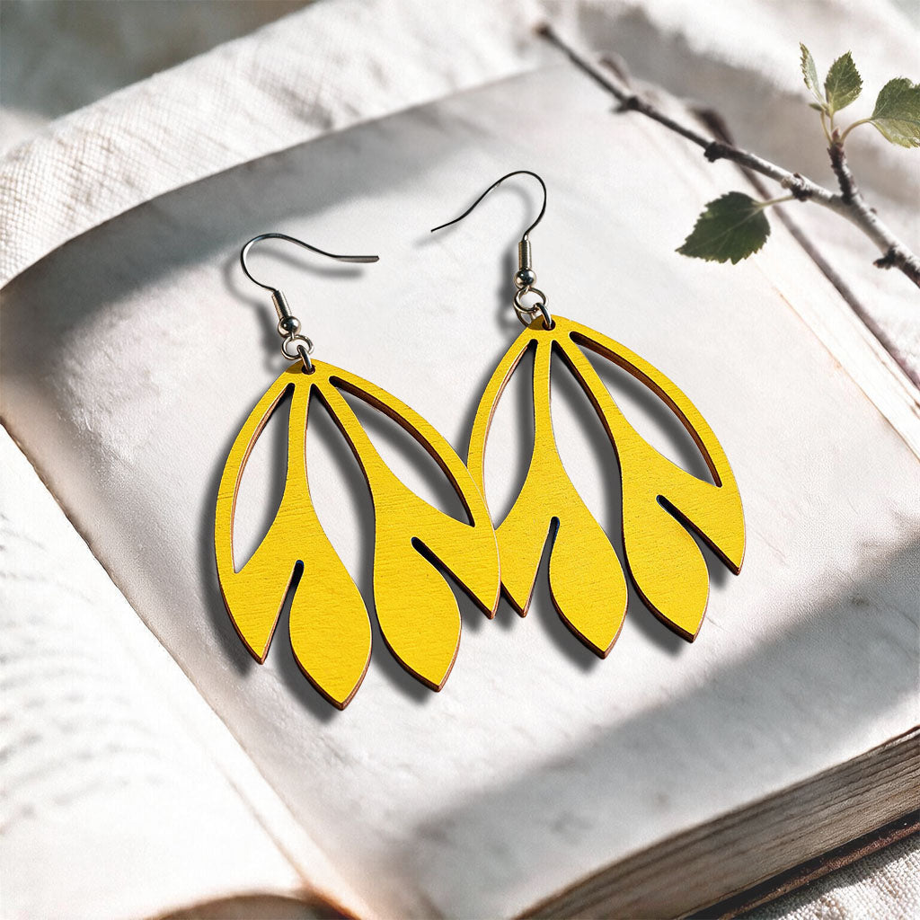 Yellow Flutter plywood earrings made in Finland, photographed on a vintage book in natural sunlight