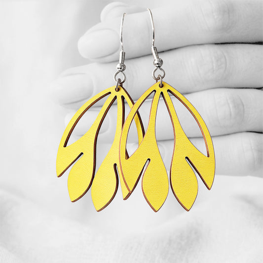 Yellow Flutter plywood earrings made in Finland, photographed on a vintage book in natural sunlight