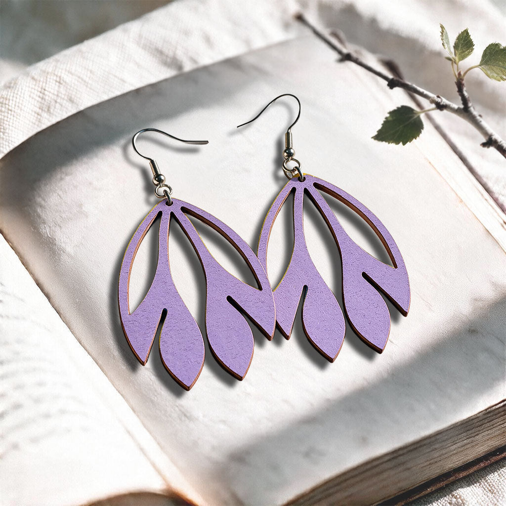 Lavender Flutter plywood earrings made in Finland, photographed on a vintage book in natural sunlight