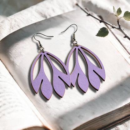 Lavender Flutter plywood earrings made in Finland, photographed on a vintage book in natural sunlight