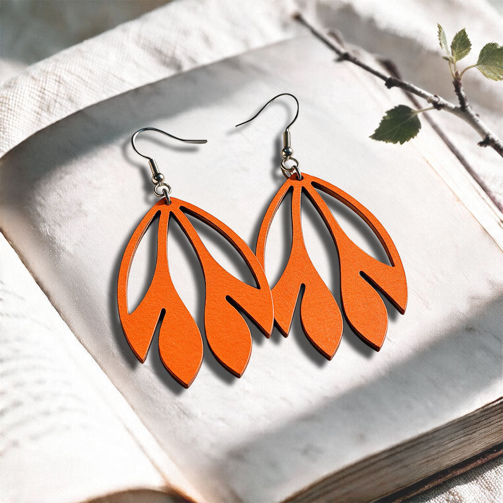 Orange Flutter plywood earrings made in Finland, photographed on a vintage book in natural sunlight