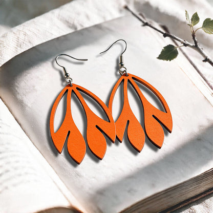 Orange Flutter plywood earrings made in Finland, photographed on a vintage book in natural sunlight