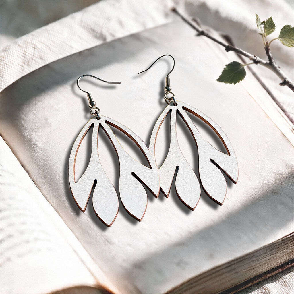 White Flutter plywood earrings made in Finland, photographed on a vintage book in natural sunlight