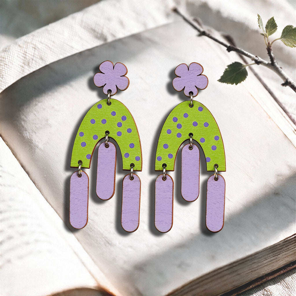 Purple and green Swinging Hems plywood earrings made in Finland, photographed on a vintage book in natural sunlight
