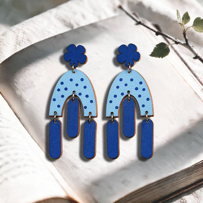 Blue Swinging Hems plywood earrings made in Finland, photographed on a vintage book in natural sunlight