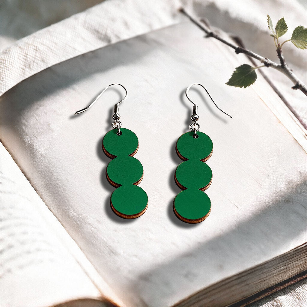 Green String of Pearls plywood earrings made in Finland, photographed on a vintage book in natural sunlight