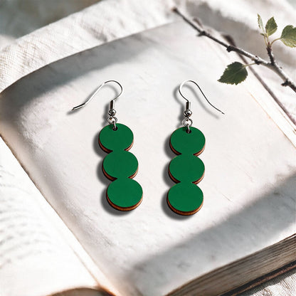 Green String of Pearls plywood earrings made in Finland, photographed on a vintage book in natural sunlight