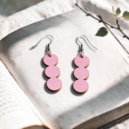 Mauve String of Pearls plywood earrings made in Finland, photographed on a vintage book in natural sunlight