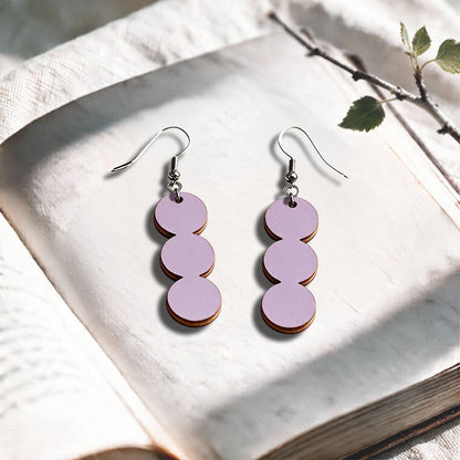 Smoke Lavender String of Pearls plywood earrings made in Finland, photographed on a vintage book in natural sunlight