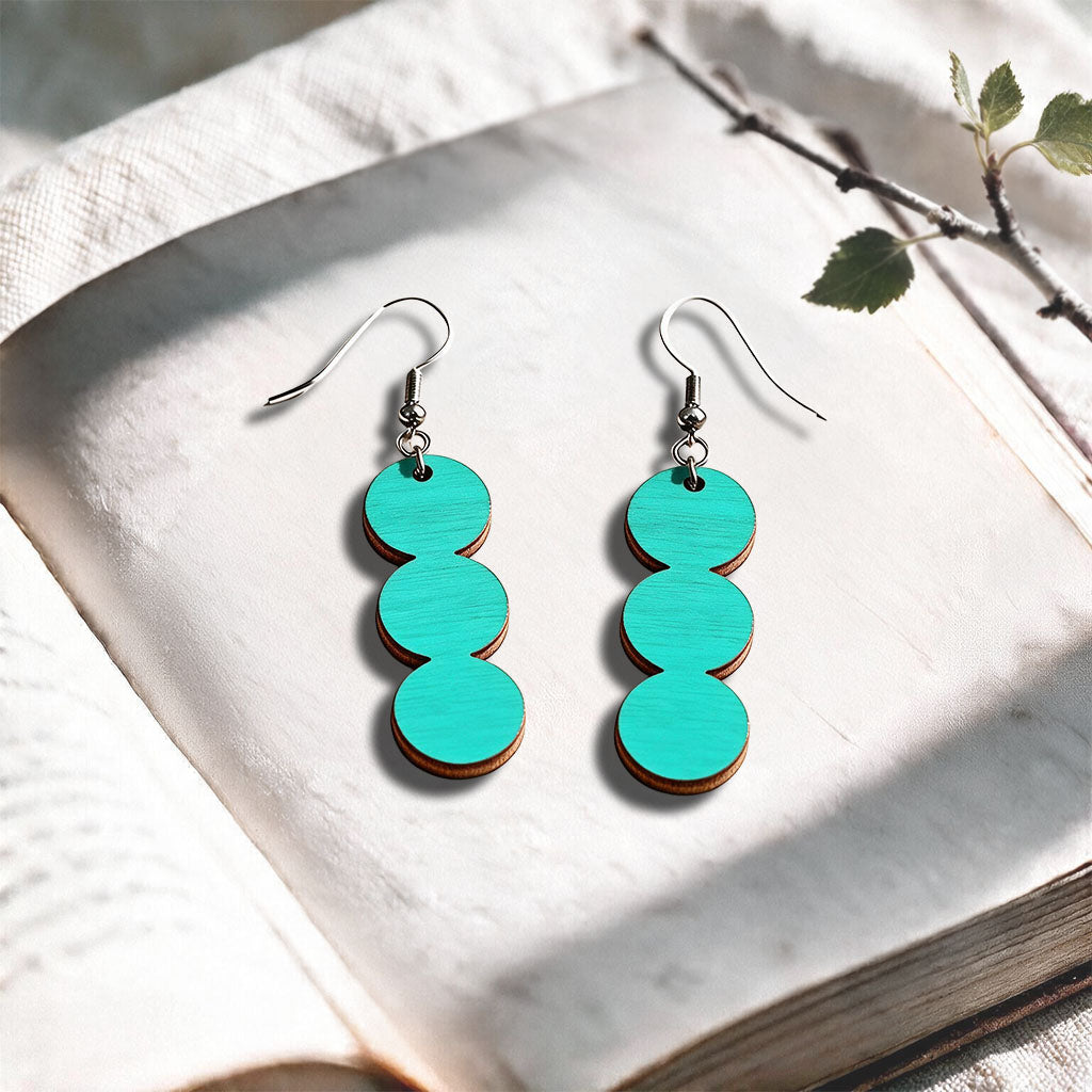 Turquise String of Pearls plywood earrings made in Finland, photographed on a vintage book in natural sunlight