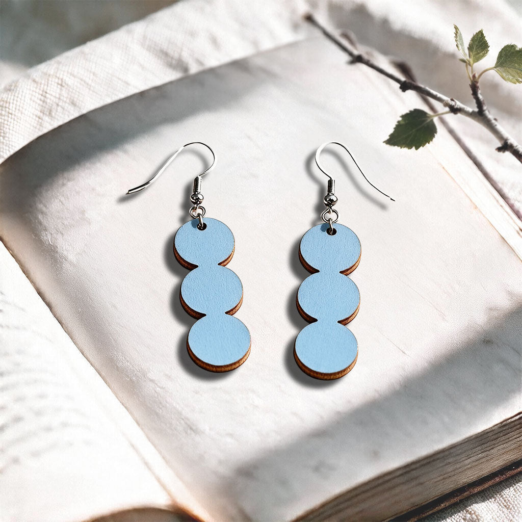 Light Blue String of Pearls plywood earrings made in Finland, photographed on a vintage book in natural sunlight