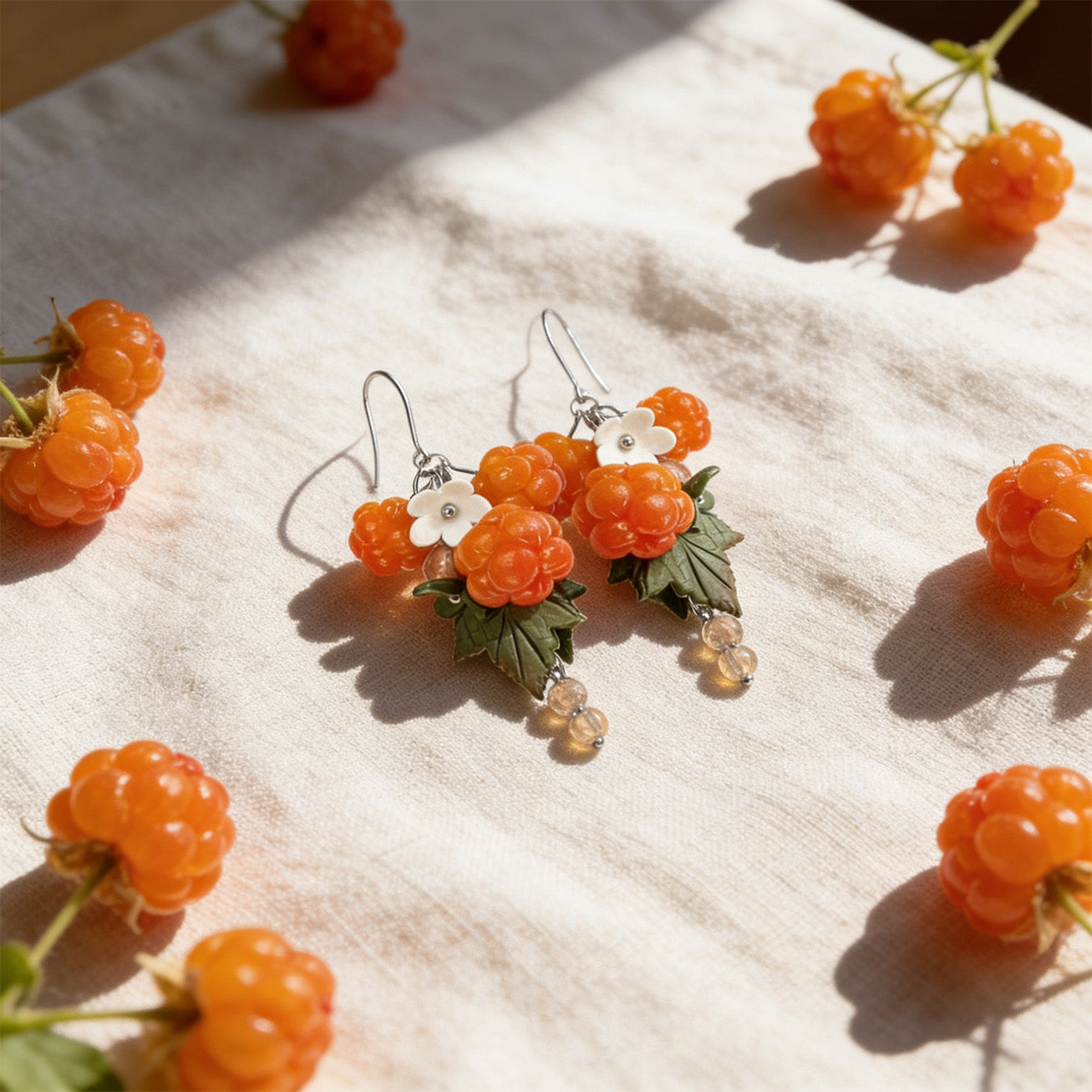 Cloudberry Marsh Earrings resting on soft forest moss among wild berries in natural outdoor light. Handmade earrings inspired by northern nature.