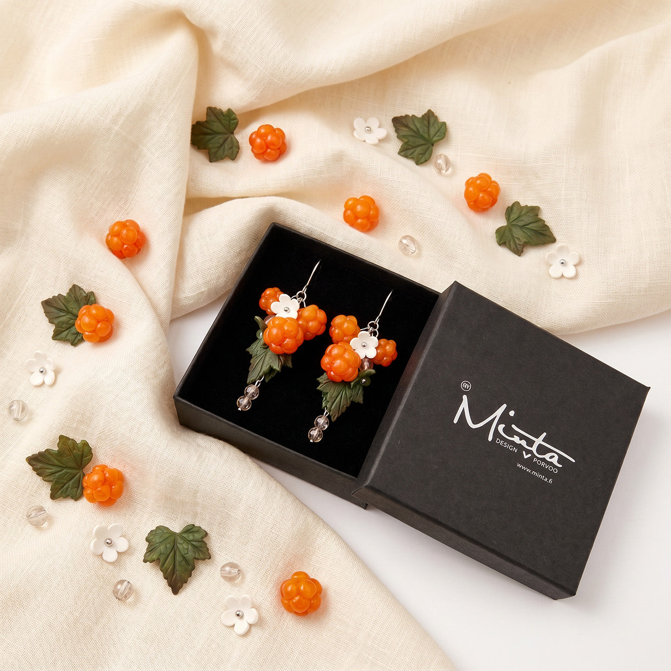 Cloudberry Marsh Earrings presented in a gift box, surrounded by natural linen fabric, fresh cloudberries, and cloudberry leaves. Handmade in Finland by byMinta.