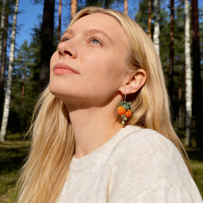 Blonde woman wearing Cloudberry Sprout Earrings in a sunlit Nordic forest. Handmade earrings inspired by the warm glow of ripe cloudberries.