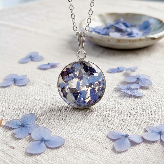 Blue hydrangea pendant necklace with preserved flowers in resin on a linen background.