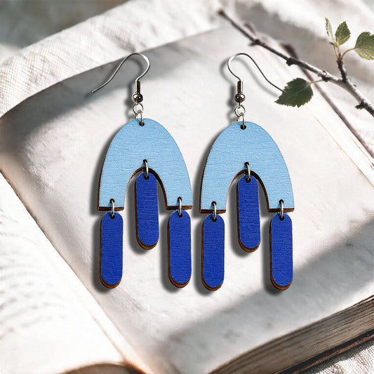 Lightblue Fluttering Hems plywood earrings made in Finland, photographed on a vintage book in natural sunlight
