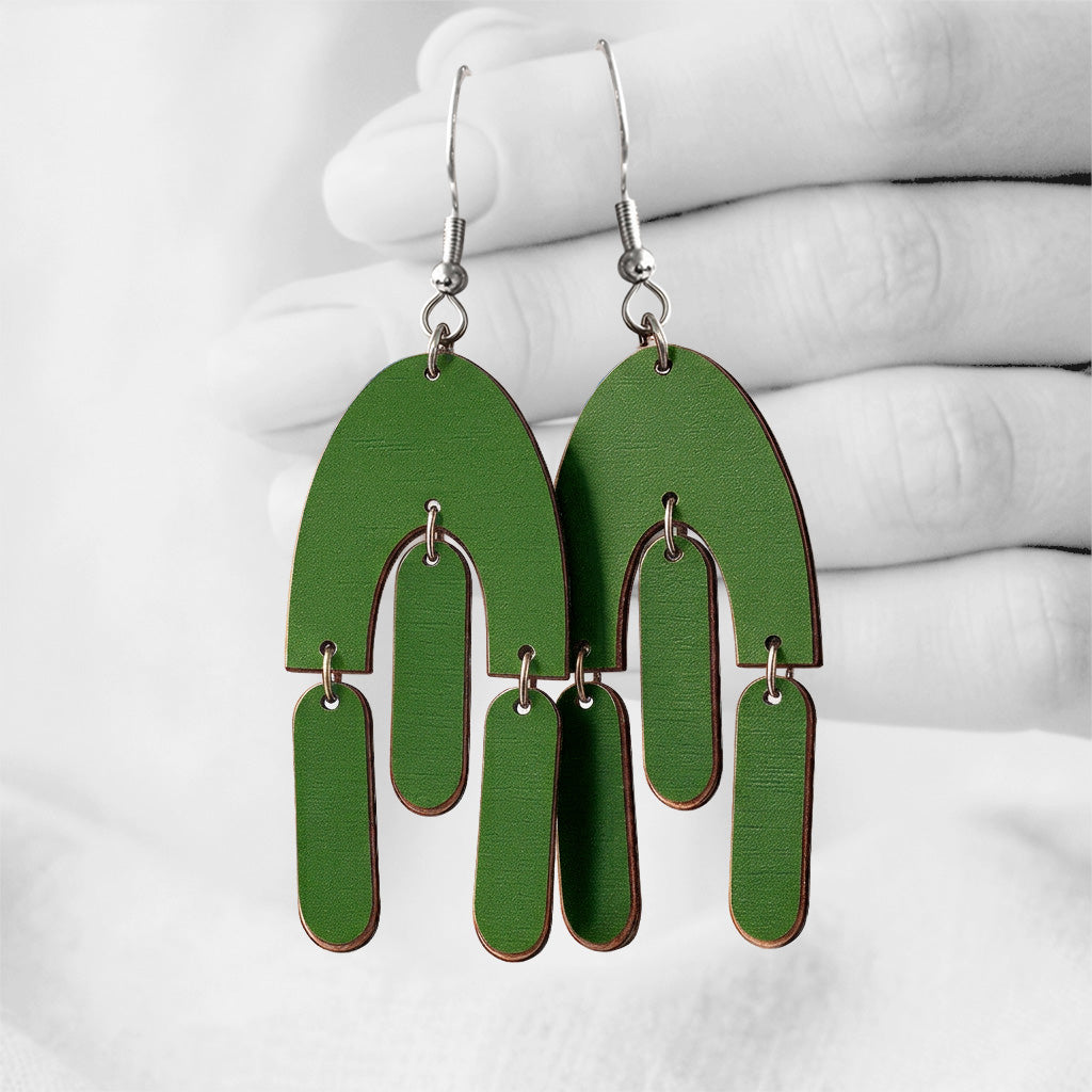 Green HulmuHelma (Fluttering Hems) plywood earrings made in Finland, photographed against a black and white background of a hand.