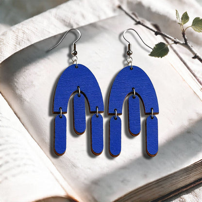 Electric blue Fluttering Hems plywood earrings made in Finland, photographed on a vintage book in natural sunlight