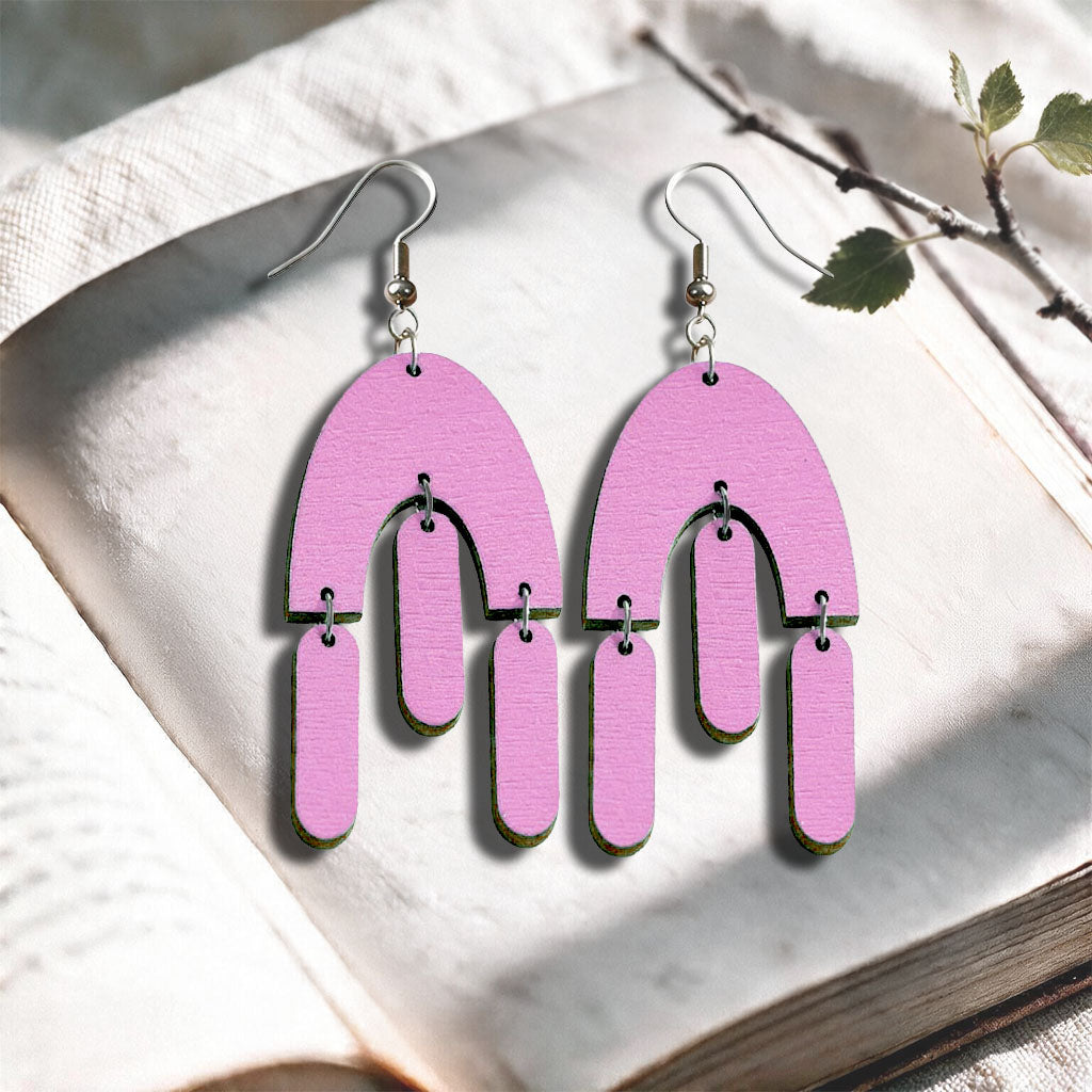 Mauve Fluttering Hems plywood earrings made in Finland, photographed on a vintage book in natural sunlight