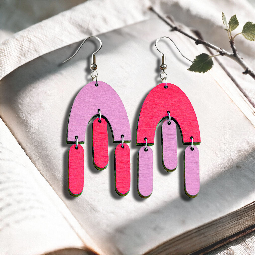 Mauve and raspberry Fluttering Hems plywood earrings made in Finland, photographed on a vintage book in natural sunlight