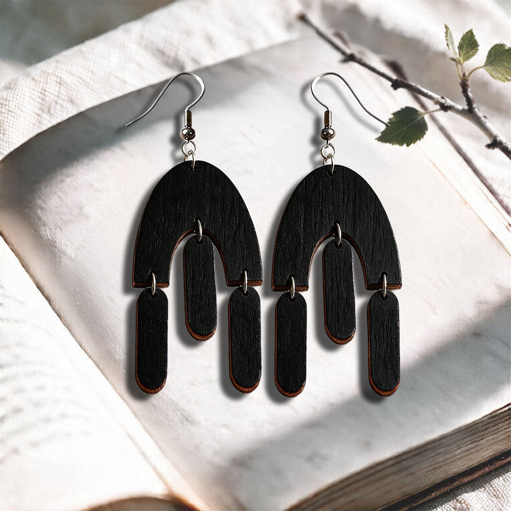 Black Fluttering Hems plywood earrings made in Finland, photographed on a vintage book in natural sunlight